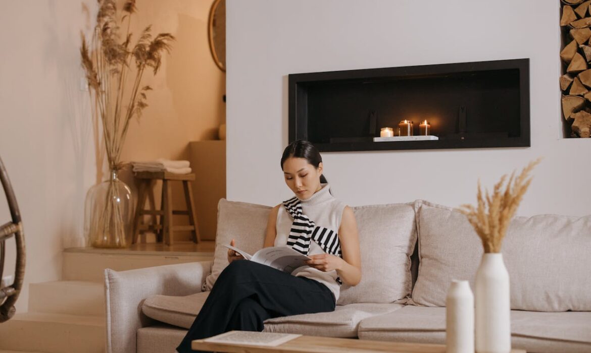 Professional woman reading Time Magazine while sitting on beige couch in modern living room with fireplace and candles
