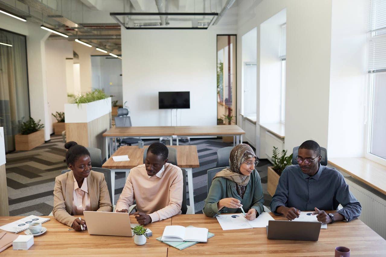Professional business team collaborating on press release distribution strategy at modern office conference table with laptops and documents